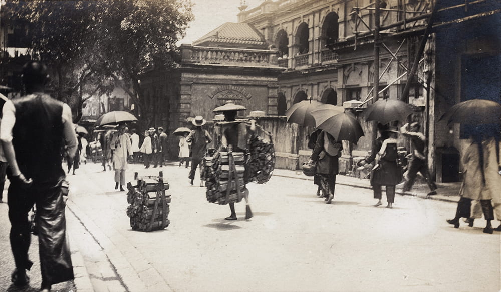 Porters carrying wood, and women with umbrellas, Hong Kong. Historical Photographs of China ref: Mi01-033.